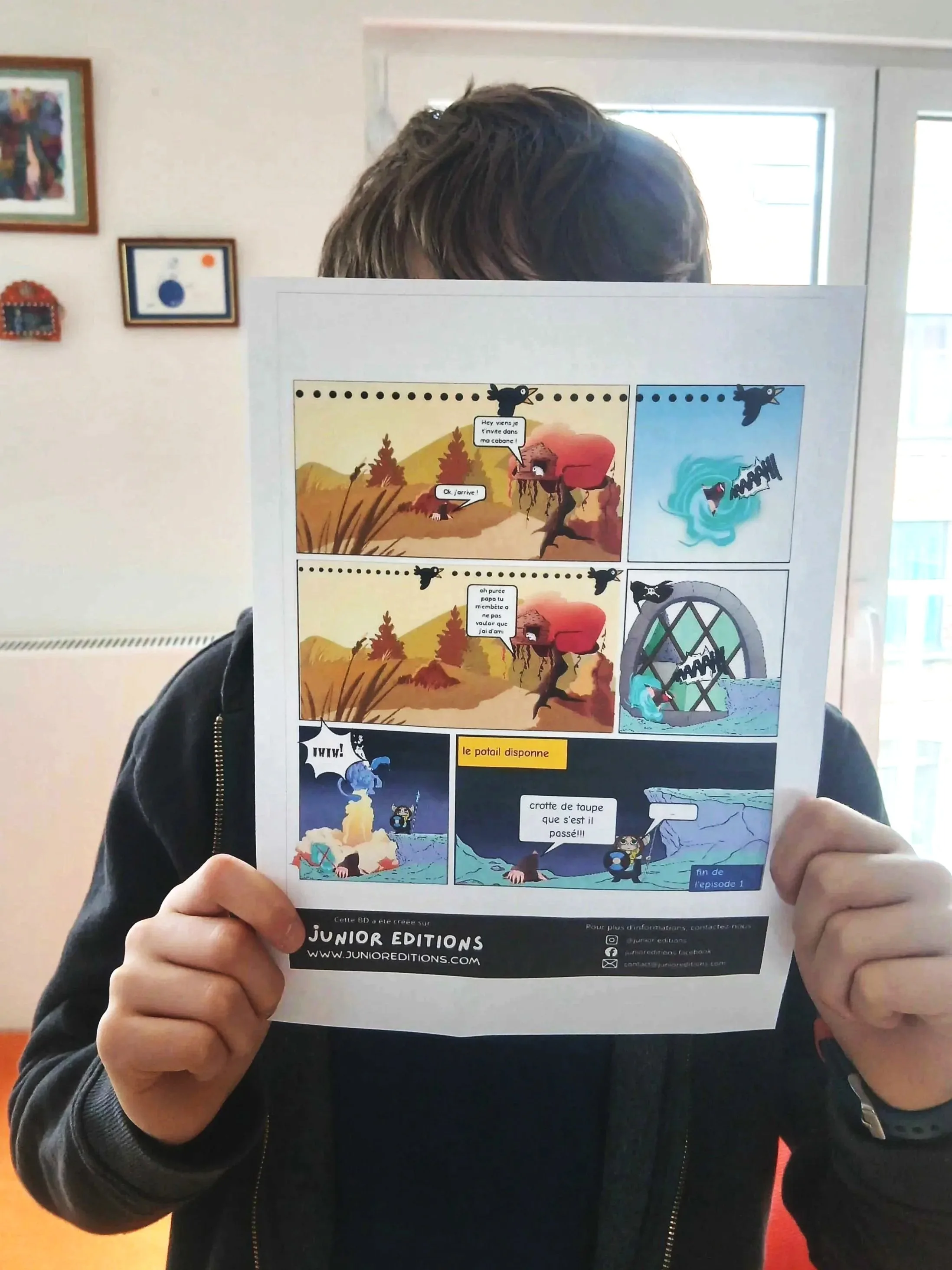 A child holds a colourful printed comic in front of their face at home.