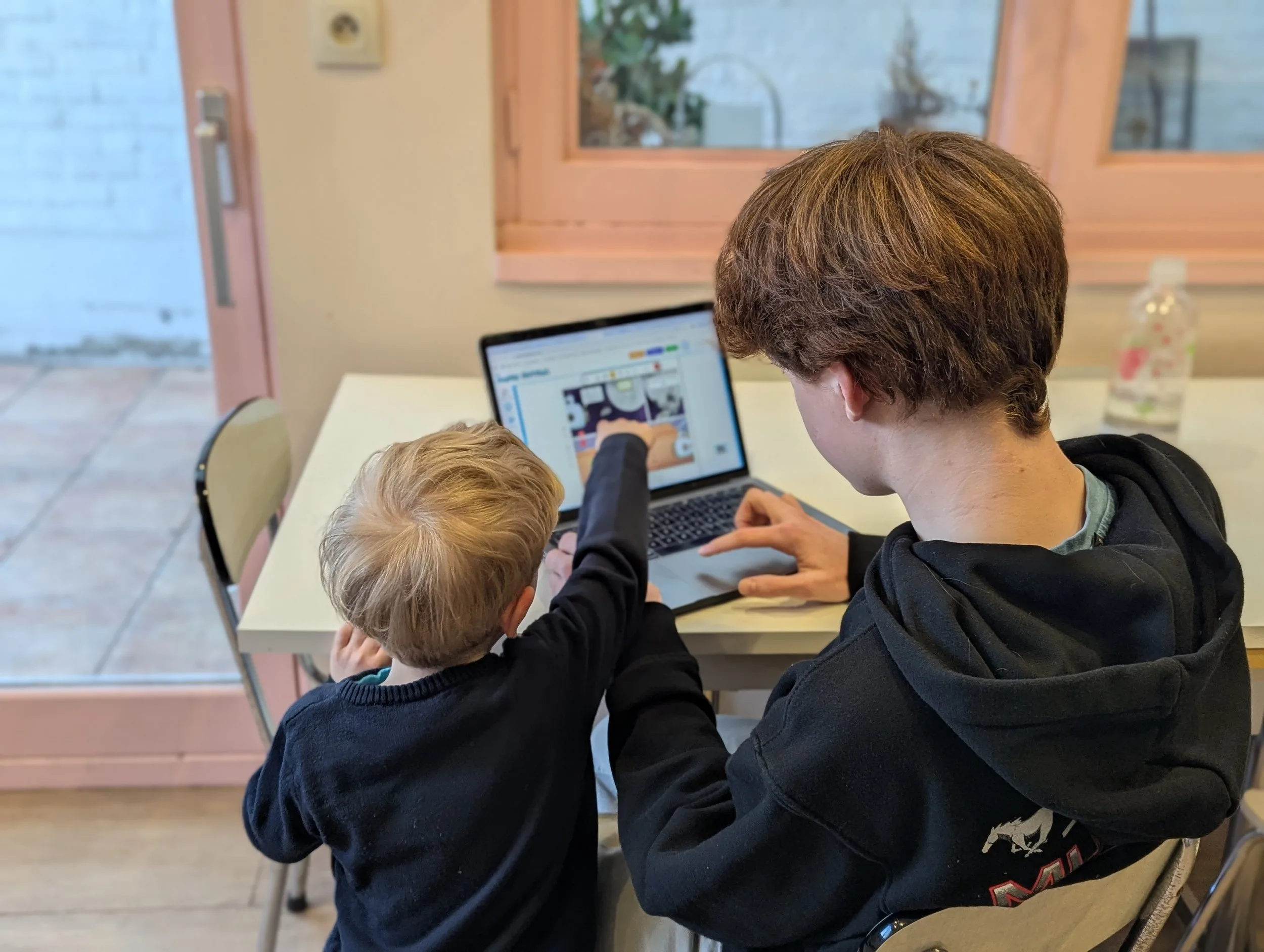Teamwork in the comic studio: two children create a story together on a laptop by a window.